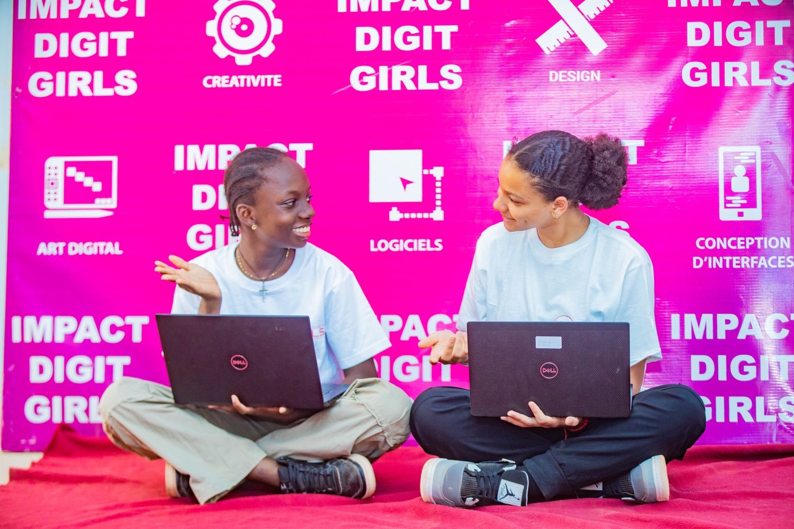 Two young women working on laptops in front of the IMPACT DIGIT GIRLS backdrop
